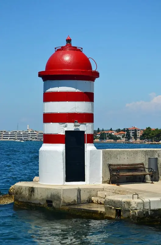 Photo of a red and white lighthouse on a harbor wall in Zadar